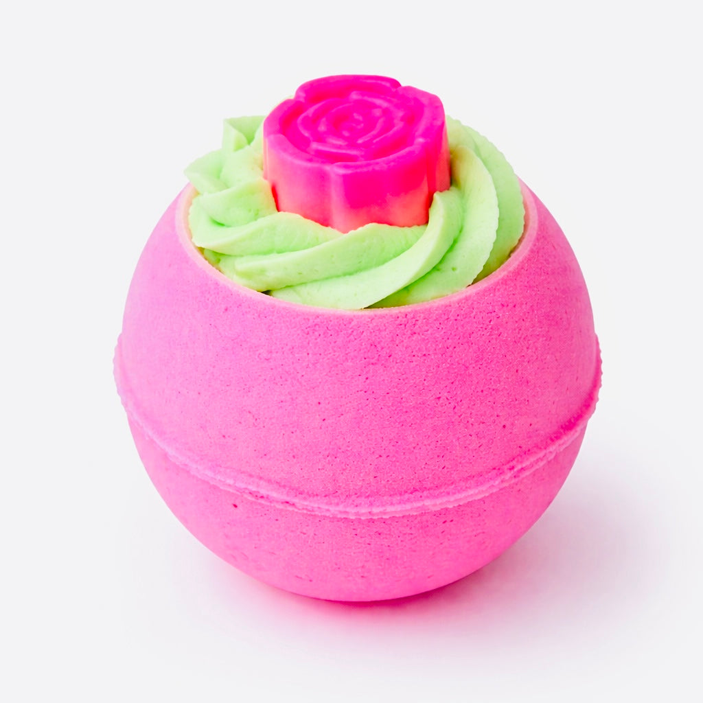 Pink bath bomb with green whipped bubble bath frosting and a rose-shaped soap topping, on a white background.