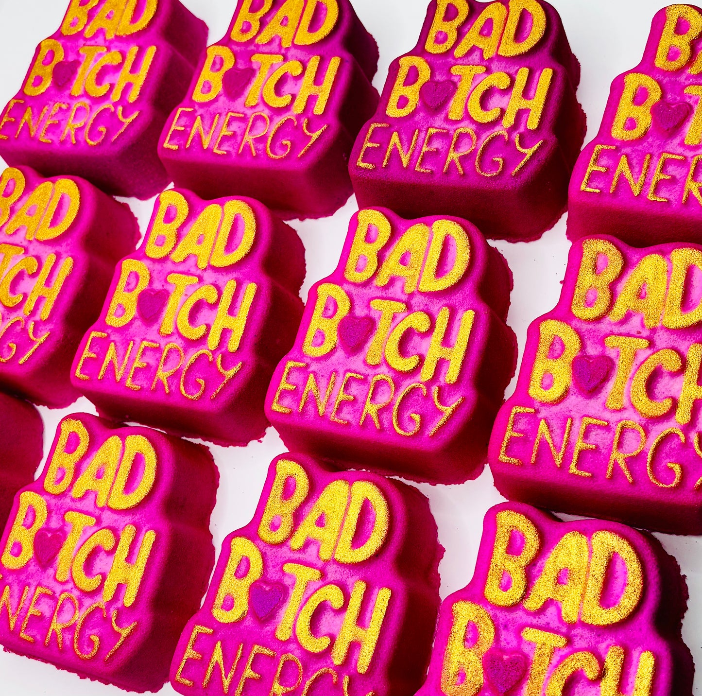 Pink and gold bath bombs with 'BAD B TCH ENERGY' text on it.