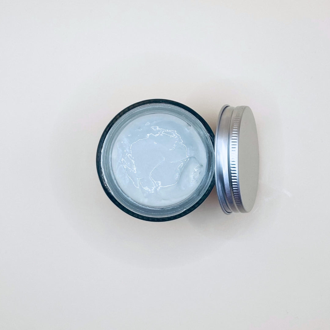 Open jar of cream with a metal lid on a white background