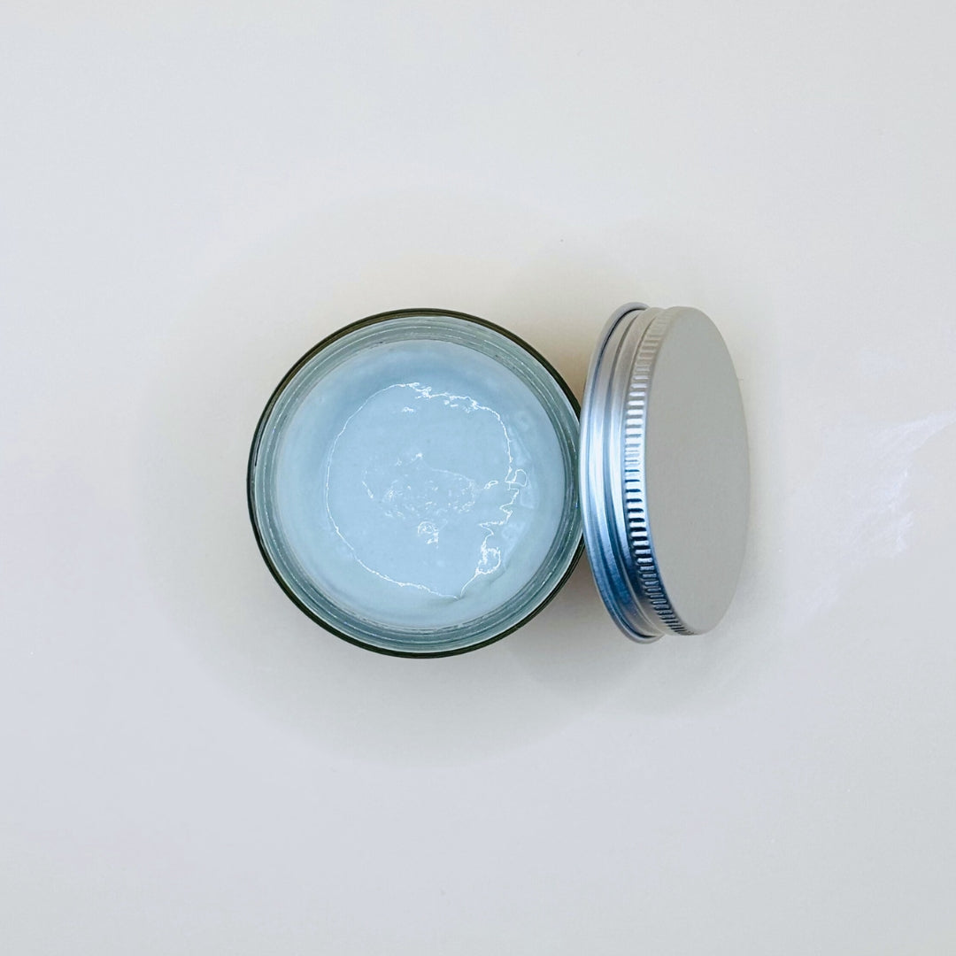 Open jar of cream with a metal lid on a white background