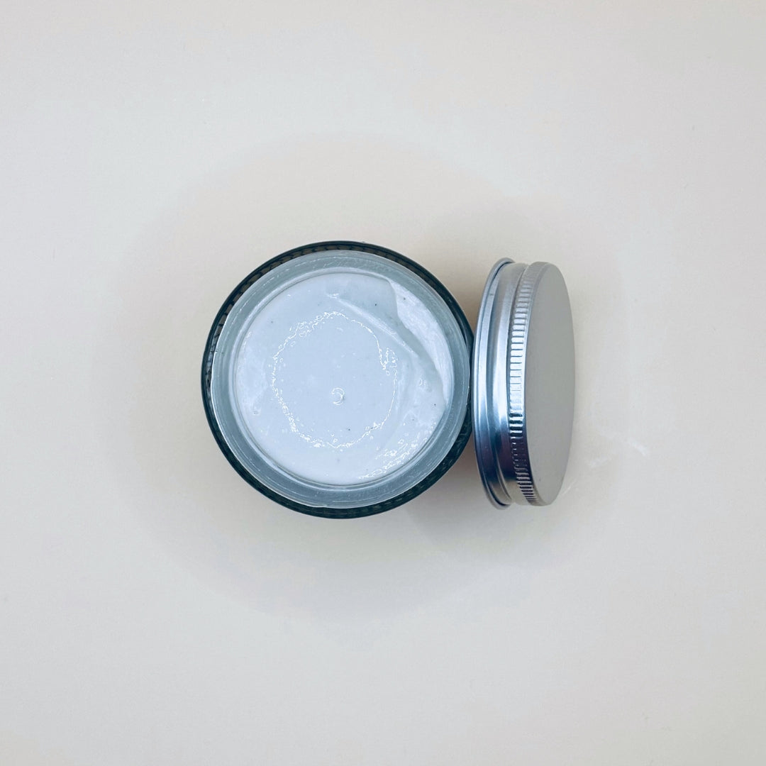 Open jar of cream with a metal lid on a light beige background