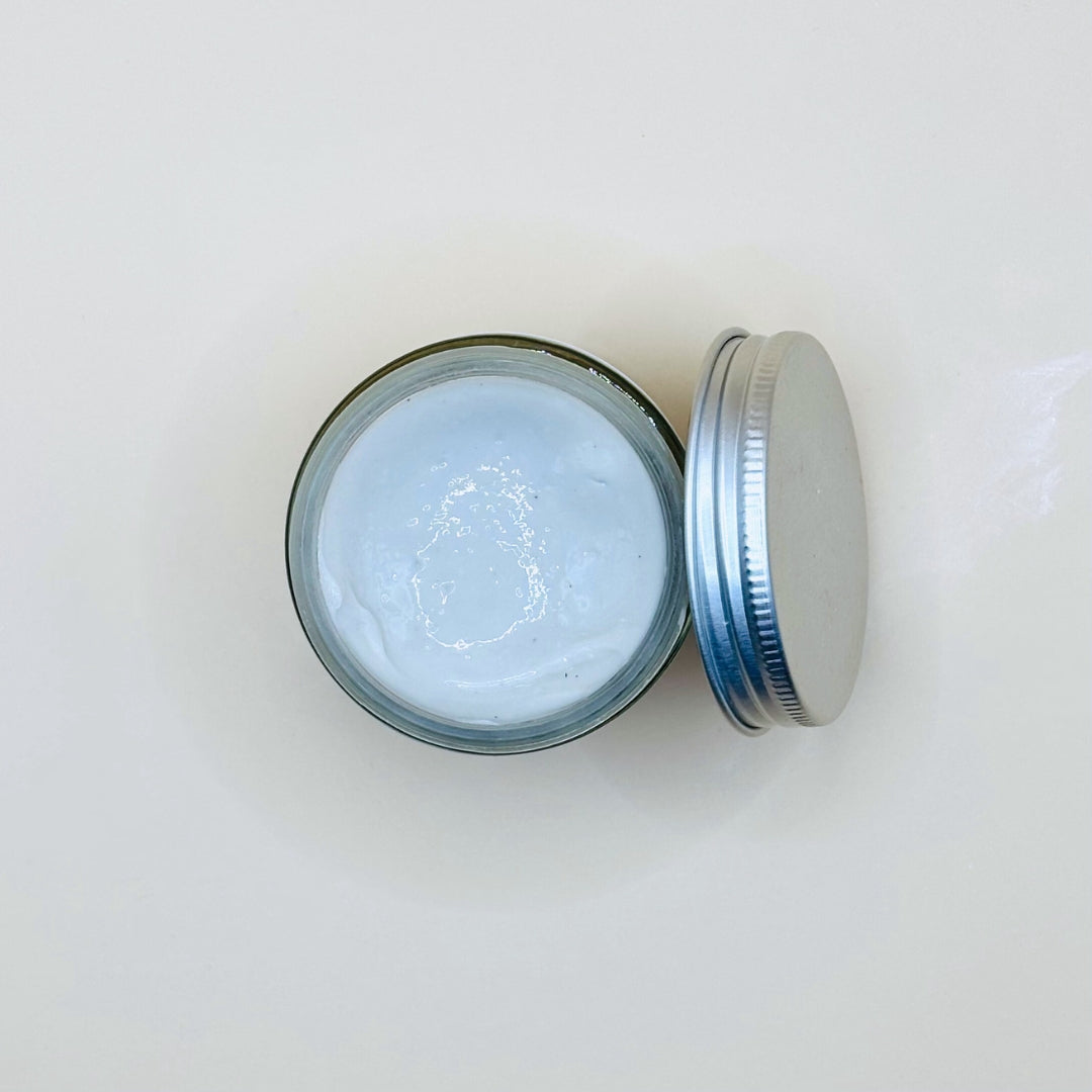 Jar of white cream with a metal lid on a light gray background