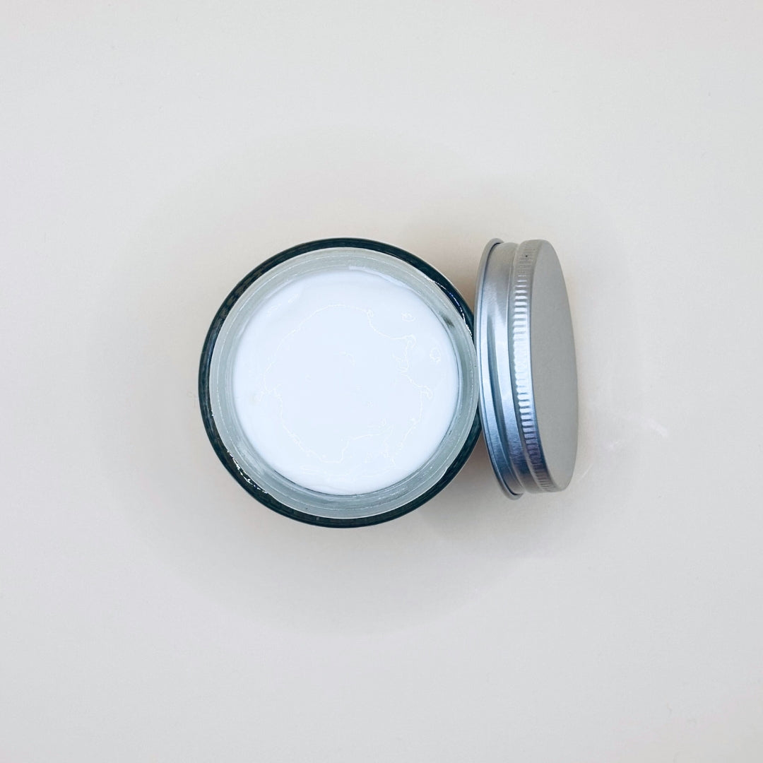 Open jar of cream with a metal lid on a light beige background