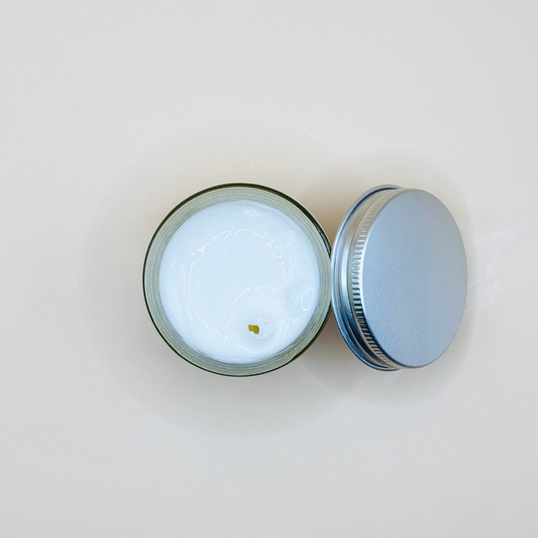 Small round container with a white candle inside, lid open on a light gray background