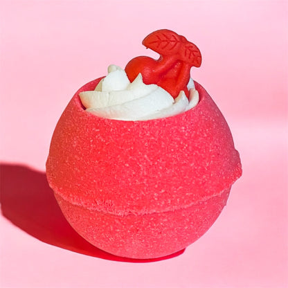 A red Berry sorbet-scented bubble bath bomb with a cherry on top, placed on a pink background.