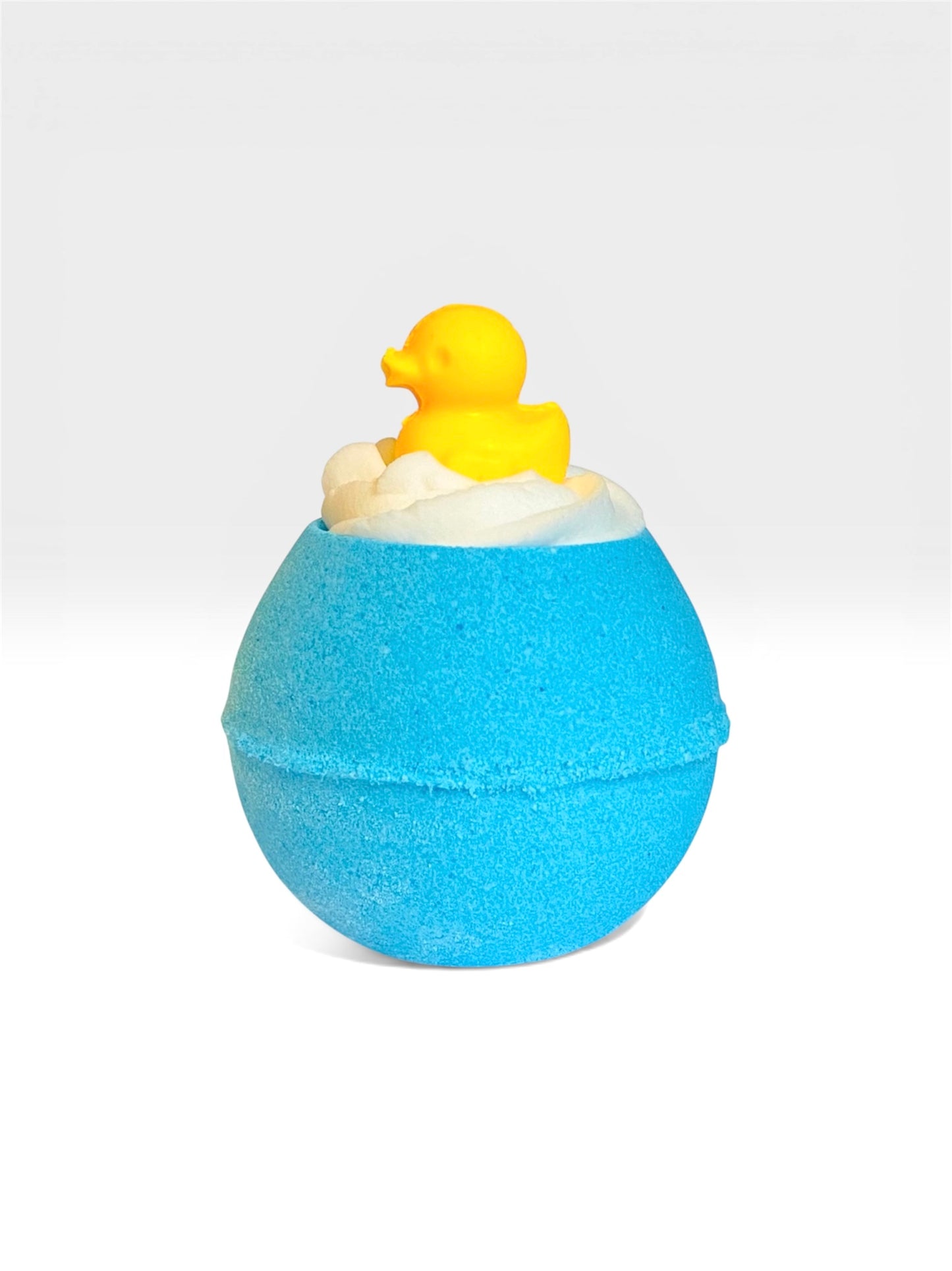 A blue round bath bomb with a white whipped bubble bath frosting on top with a a duck shaped soap on top, on a white background.