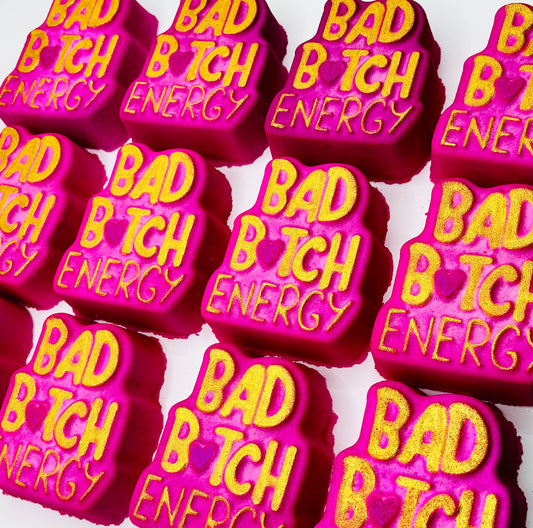 Pink and gold bath bombs with 'BAD B TCH ENERGY' text on it.