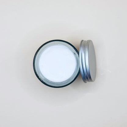 Open jar of cream with a metal lid on a light beige background